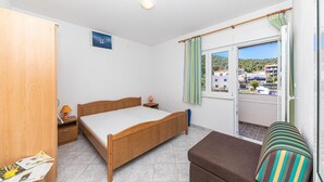 Un dormitorio con una cama de madera, una mesita de noche, una lámpara, una ventana con cortinas y vistas a edificios.