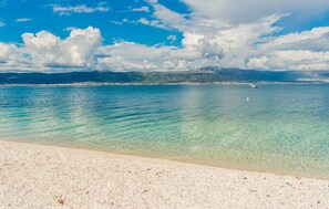 A beach with clear turquoise water, a boat in the distance, and a mountainous backdrop. - Amazing apartment in Slatine (Slatine)
