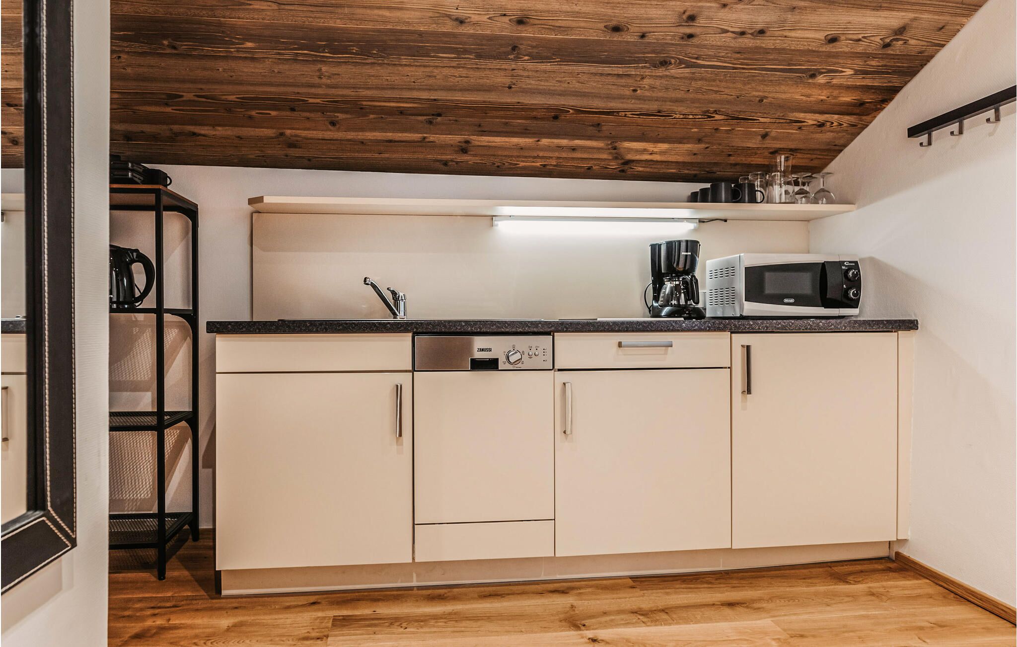 Een kleine keuken met houten plafond, een inbouwmagnetron, koffiezetapparaat en een spoelbak.