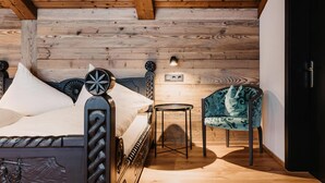 Une chambre avec un plafond en bois, un lit doté d’une tête de lit en métal, une petite table ronde, un fauteuil recouvert d’un tissu vert et un luminaire fixé au mur.
