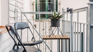 Un balcon avec un pot de fleurs, deux chaises noires et une petite table en bois.