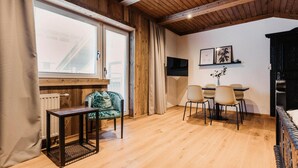 Une pièce chaleureuse avec un plancher en bois, un coin repas comprenant des chaises et une table, ainsi qu’une fenêtre avec des stores.