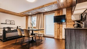 Una habitación moderna con techo de madera, un comedor con mesa y sillas, una cama con cabecera, un televisor de pantalla plana en la pared y una cocina con pileta y estufa.
