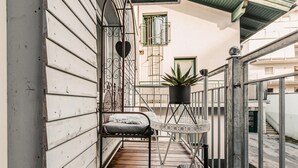 Un balcón con suelo de madera, un banco acolchado, una planta en maceta y una barandilla decorativa de metal.
