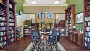 A library with bookshelves, two leather chairs, a round table, and a patterned rug. - Beautiful 3 BR 2.5 Bath Paseo Townhome in a Quad (Fort Myers)