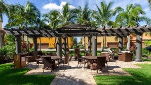 An outdoor patio area with tables and chairs, surrounded by palm trees and a pergola. - Beautiful 3 BR 2.5 Bath Paseo Townhome in a Quad (Fort Myers)