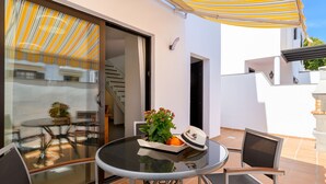 A glass-enclosed patio with a round table, two chairs, a potted plant, and a hat on the table. - Casa Grumete, moderno y actual (Playa Honda)