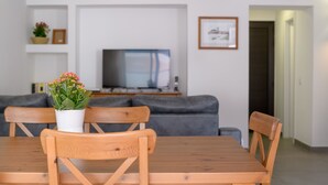A dining area with a wooden table and chairs, a potted plant, a grey sofa, and a television in the background. - Casa Grumete, moderno y actual (Playa Honda)