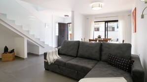 A modern living room with a grey sofa, a staircase, and a dining area with a table and chairs. - Casa Grumete, moderno y actual (Playa Honda)