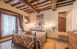 Un dormitorio con cama, ventana con cortinas, techo de madera, un cuadro en la pared y un armario de madera.