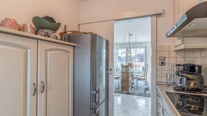 A kitchen with white cabinets, a stainless steel refrigerator, a stove, and a dining area visible through an open door. - 2 bedroom beautiful apartment in Friedrichskoog (Friedrichskoog)