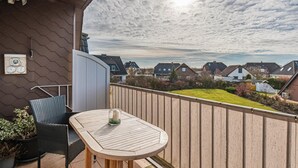 A balcony with a wooden table and chairs, a potted plant, and a view of houses in the distance. - 2 bedroom beautiful apartment in Friedrichskoog (Friedrichskoog)