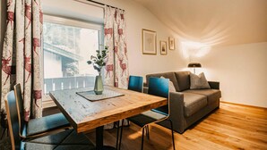 A cozy living room with a wooden dining table, blue chairs, a grey sofa with cushions, and a floor lamp. - gemuetliche Ferienwohnung (Wagrain)