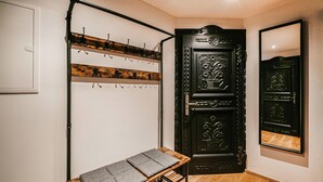 A room with a black ornate door, a coat rack with hooks, a small table with folded mats, and a mirror on the wall. - gemuetliche Ferienwohnung (Wagrain)