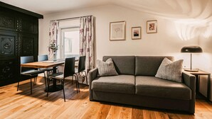 A living room with a sofa, a dining table with chairs, a lamp, and a window with curtains. - gemuetliche Ferienwohnung (Wagrain)