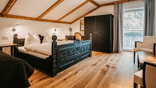 A bedroom with a wooden ceiling, a bed with a decorative headboard, a wardrobe, a desk, and a window with curtains. - gemuetliche Ferienwohnung (Wagrain)