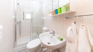 Un baño con ducha envuelta en vidrio, inodoro blanco, lavamanos con dispensador de jabón y toallero con toallas.