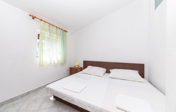 Un dormitorio con una cama individual, una mesita de noche y una ventana con cortinas translúcidas.
