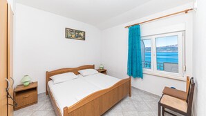 Un dormitorio con una cama de madera, una mesita de noche, una silla, una ventana con vista al mar y un cuadro en la pared.