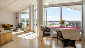 Ein geräumiges Zimmer mit großen Fenstern, einer Holzbalkendecke und Meerblick.