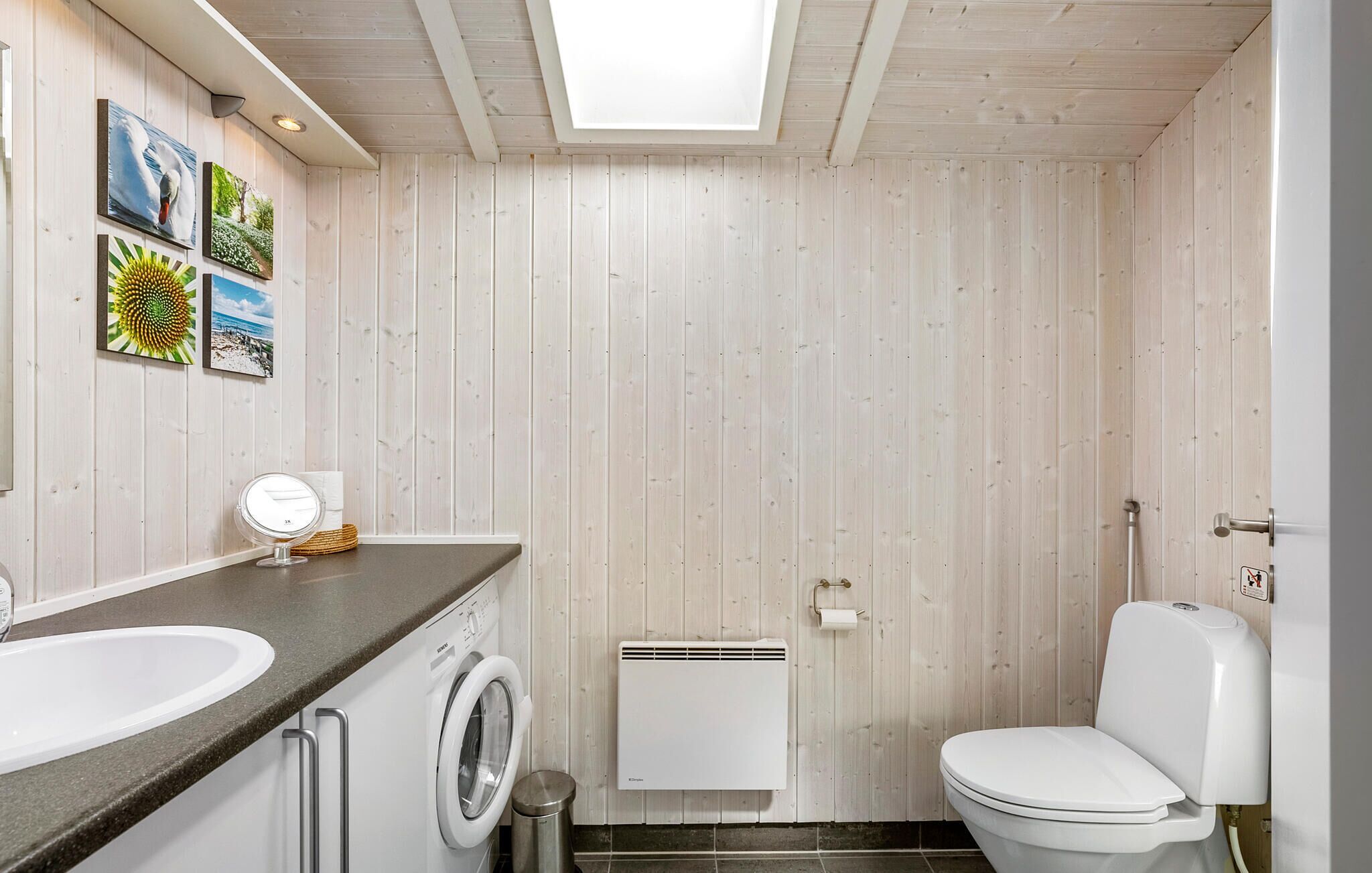 A compact bathroom with a washing machine, toilet, and a skylight.
