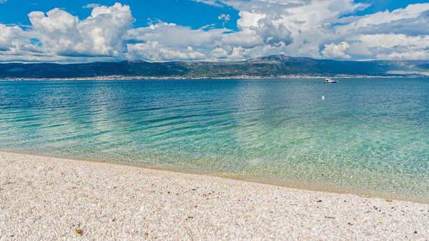 A beach with clear turquoise water, a distant mountain range, and a small boat in the distance. - 1 bedroom beach front apartment in Slatine (Slatine)