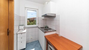A compact kitchen with a window, white cabinets, a stove, and a small wooden table. - 1 bedroom beach front apartment in Slatine (Slatine)