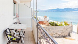 A balcony with a table and chairs, overlooking a coastal view with mountains in the distance. - 1 bedroom beach front apartment in Slatine (Slatine)