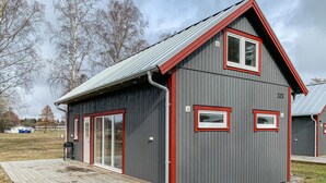 A small, single-story building with a sloped roof and red trim. It has a large sliding glass door and two windows with red frames.