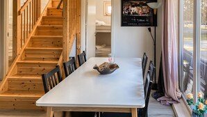 A wooden staircase leading to a bedroom, a dining table with chairs, and a poster on the wall.