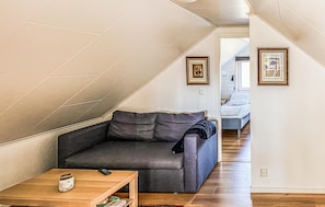 Une chambre de style loft avec un canapé gris, une petite table en bois et un lit recouvert d’une couette blanche.