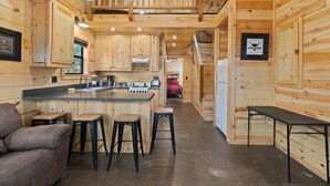 L’intérieur d’un chalet en bois comprend une cuisine, des tabourets de bar, un canapé et une table à manger.
