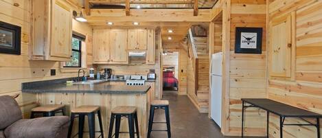 Interior de una cabaña de madera con cocina, taburetes de bar, sofá y una mesa de comedor.