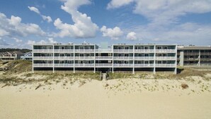 A multi-story hotel with a flat roof and balconies, located on a sandy beach with a clear sky. - Stunning Top-Floor Oceanfront Condo! Pools & New Step in Shower and More! (Nags Head)