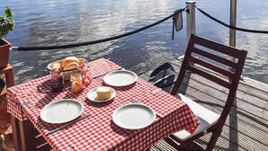 A table set with a checkered tablecloth, plates, butter, bread, and condiments on a boat deck with a rope barrier and a view of calm water.