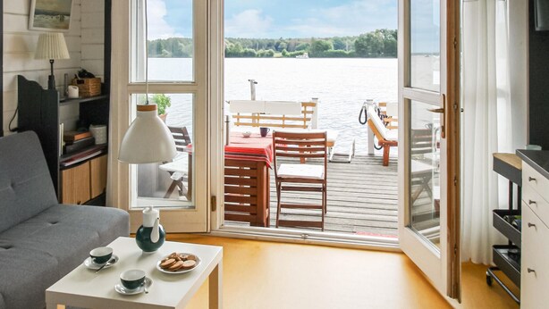 A cozy room with a sofa, a small table with a teapot and cookies, and a view of a wooden deck with a table and chairs overlooking a lake.