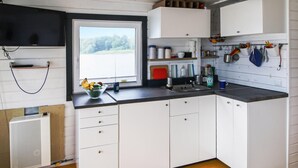 A kitchen with white cabinets, a window with a view of trees, a sink, and various kitchen utensils on the wall.