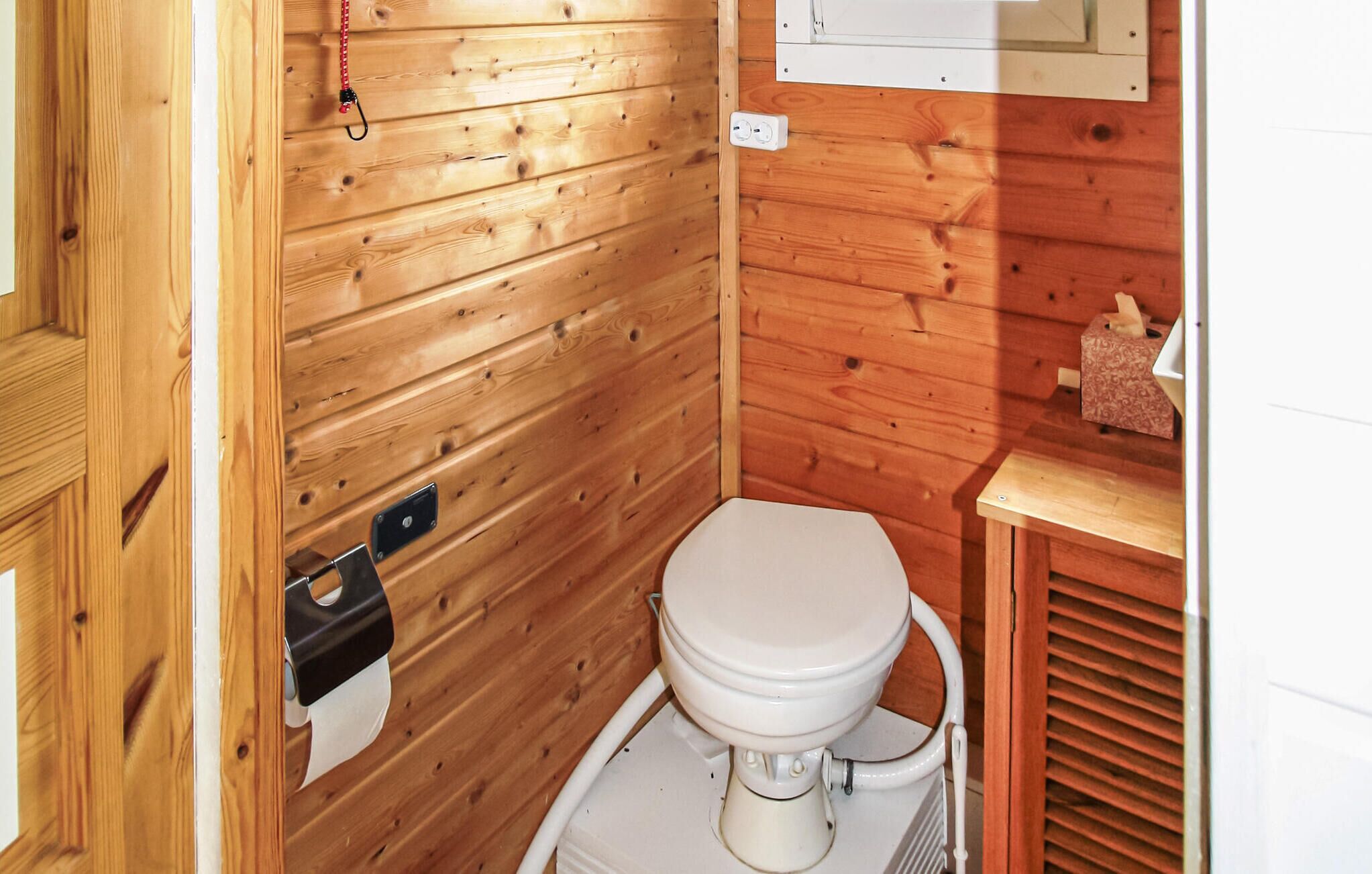 Ein kleines, kompaktes Badezimmer aus Holz mit Toilette, Handlauf und Holzschrank mit Taschentuchbox.