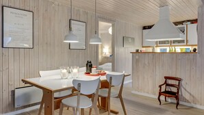 Ett modernt matområde med ett vitt bord, fyra stolar och två hänglampor. På väggen hänger en inramad affisch och i hörnet står en trästol.