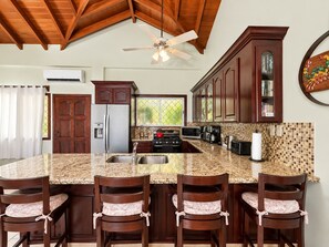 A kitchen with a granite countertop, wooden cabinets, a refrigerator, a stove, and a ceiling fan. - Beach House-Hopkins Belize- 4BR (Hopkins)