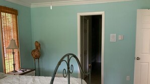 Une chambre à coucher avec un lit, un ventilateur de plafond, une porte et une fenêtre avec des stores.