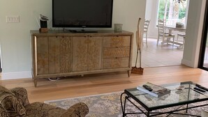 Un salon avec un téléviseur à écran plat posé sur un meuble en bois, des canapés à motifs et une table basse en verre.