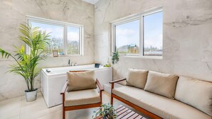 A bathroom with a bathtub, two chairs, and a sofa. There are two windows with views of the outside.