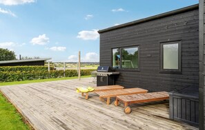 Una casa moderna negra con terraza de madera, una parrilla y vistas al campo.