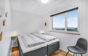 Un dormitorio con cama, mesitas de noche, una silla, ventana con vistas y una lámpara en el techo.