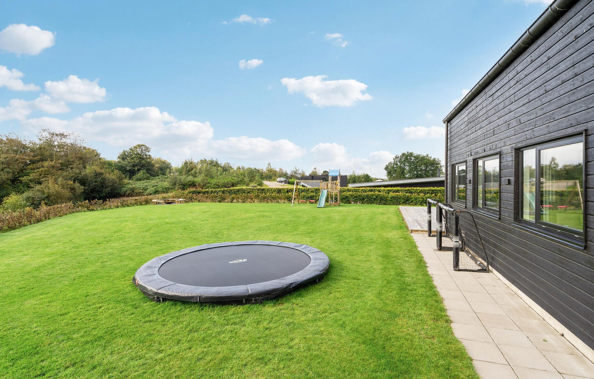 Ein Garten mit Trampolin, Spielhaus aus Holz und einer Hecke.