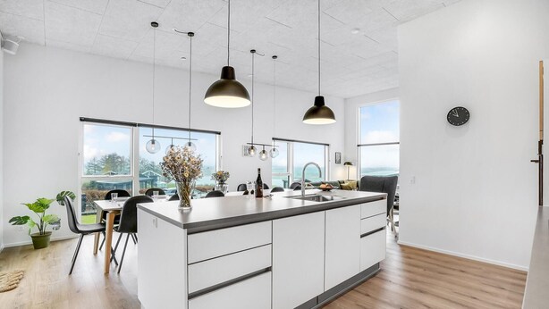 A modern kitchen with a large island, pendant lights, and a view of the outdoors.