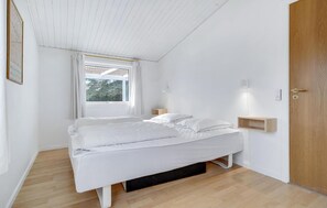 A bedroom with a bed, a window, a door, and a wall-mounted light fixture.