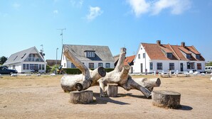 Een beeldhouwwerk van houtblokken in een landelijke omgeving, met huizen op de achtergrond.