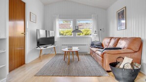 Een woonkamer met een televisie, een leren bank, een bijzettafeltje en een raam met uitzicht op gebouwen.